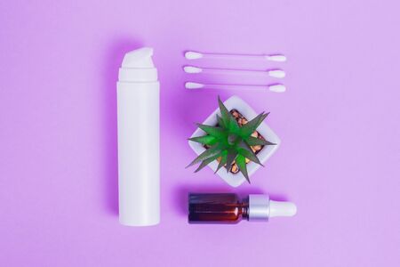 Moisturizing face cream with collagen and mucin of a snail for the skin of the face against wrinkles and acne in a white package with a pump and face serum in a glass bottle with makeup sticks and green succulent on a purple backgroundの写真素材