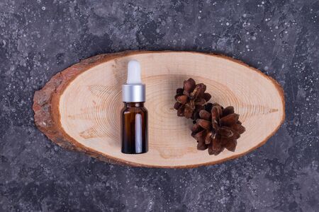 Moisturizing serum with collagen and mucin of a snail for face skin against wrinkles and acne in a glass bottle on a wooden stand and cones on a gray tableの写真素材