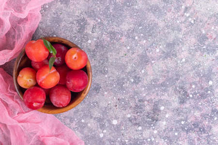 Ripe plums in a wooden plate with dew with a pink napkin on a gray concrete background