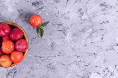 Ripe plums in a wooden plate on a gray background