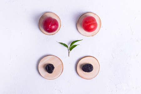 Ripe red plum on a wooden stand with prunes, dried plum for human health on a white textured backgroundの写真素材