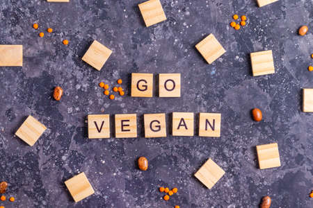Inscription go vegan in wooden letters with raw beans and orange lentils on a gray concrete...