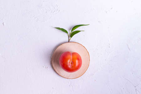Ripe red plums with green leaves from a tree on a white textured background copyspace