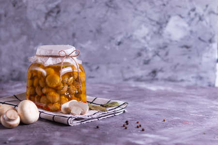 Fermented canned champignon mushrooms in a glass jar with garlic, bay leaf and a white napkinの写真素材