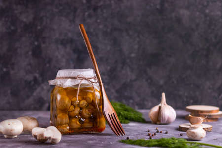 Fermented canned champignon mushrooms in a glass jar with garlic, bay leaf and dill with wooden coastersの写真素材