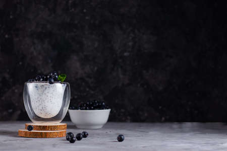 Chia pudding with mint and blueberries in glasses on a wooden stand with a plate of blueberries on a dark backgroundの写真素材