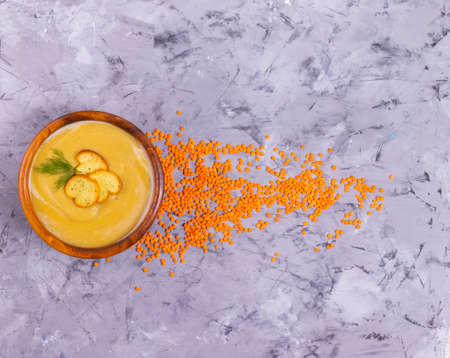 Lentil and pumpkin cream soup with dill in a wooden plate with a wooden spoon with orange lentils scatteredの写真素材