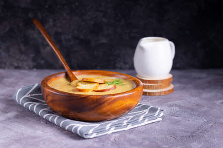 Lentil and pumpkin cream soup with dill in a wooden plate with a wooden spoon with creamer on wooden coasters on a gray backgroundの写真素材