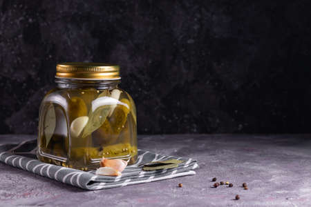 Fermented canned cucumbers with bay leaf, garlic and dill in a glass jar on a gray backgroundの写真素材