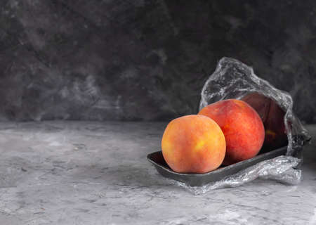 Fresh peaches in a plastic container with cling film on a dark backgroundの写真素材