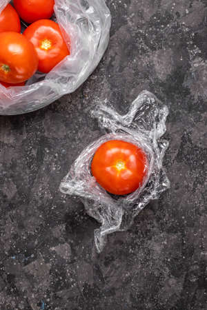 Tomato in plastic cling film with a package of tomatoes on a gray table