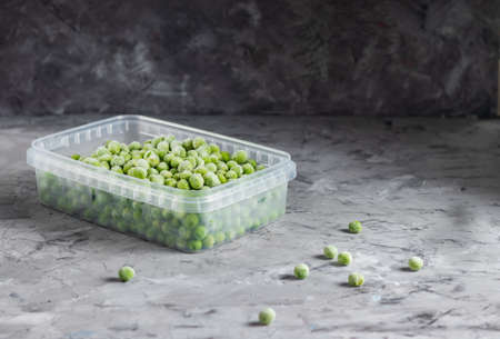 Frozen green peas in a transparent plastic container on a dark backgroundの写真素材