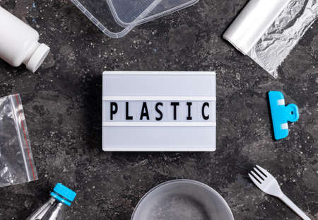 Plastic inscription on gray background with plastic bags, clip, fork and container
