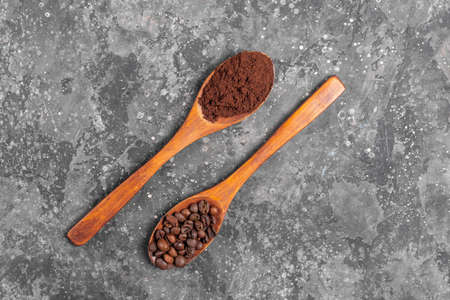 Coffee beans and ground coffee in wooden eco spoons on gray backgroundの写真素材