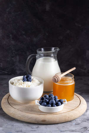 Grain cottage cheese in a white plate with blueberries with sour cream, milk and honey on a wooden standの写真素材
