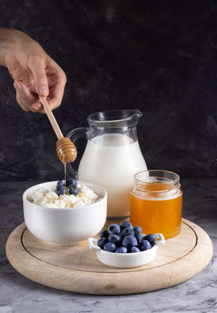 Honey pouring on grained curd with blueberries in a white plate on a gray backgroundの写真素材