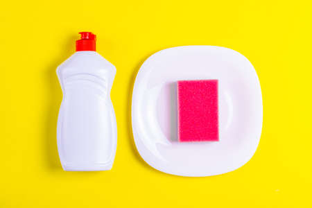 Dishwashing liquid, plate and pink sponge on yellow background