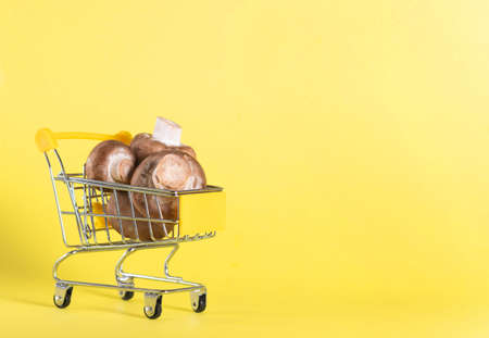 Brown champignons in grocery trolley on yellow backgroundの写真素材