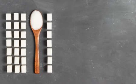 Sugar lumps with a wooden eco spoon filled with loose sugar on a gray background on a gray background for World Diabetes Day November 4の写真素材