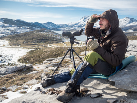 Explorer looking  in the mountains with binoculars and telescope under blue skyの写真素材