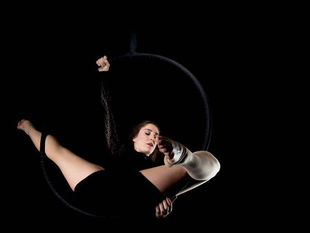 Graceful aerial dancer woman doing her performance with a hoop isolated on blackの写真素材