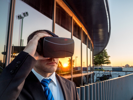 Businessman using virtual reality glasses at sunset in a business center. New technology for business concept.の写真素材