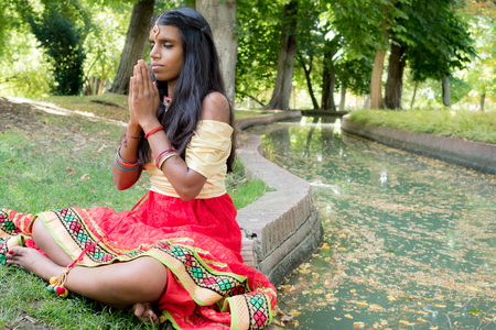 Beautiful young indian woman praying and meditating in the park. Hinduism religion. Radja Yoga practiceの写真素材