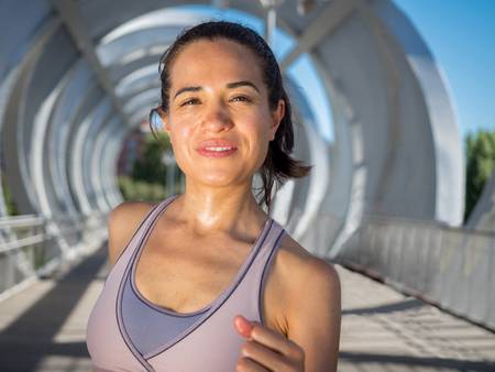 Female Runner smiling and running on a modern bridge. Wellness and healthy lifestyle concept.の写真素材