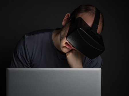 Tired addicted man to technology  using virtual reality headset at night. Technology addiction and mental disorders concept.の写真素材