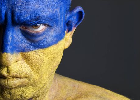 Man with his face painted with the flag of Ukraine.  The man is serious and photographic composition leaves only half of the face.の写真素材