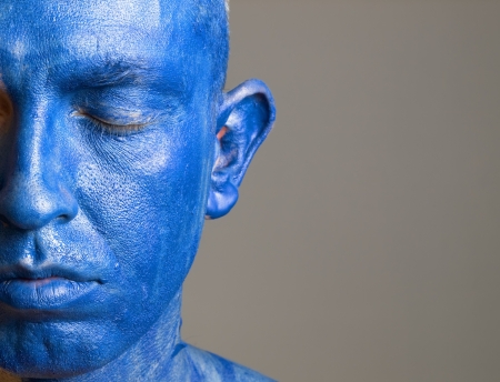 Man and his face painted with color blue. The man is closed eyes and photographic composition leaves only half of the face.の写真素材