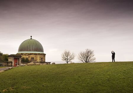 Dome building in Calton Hill, Edinburgh  There are two leafless trees and one person, the sky is...