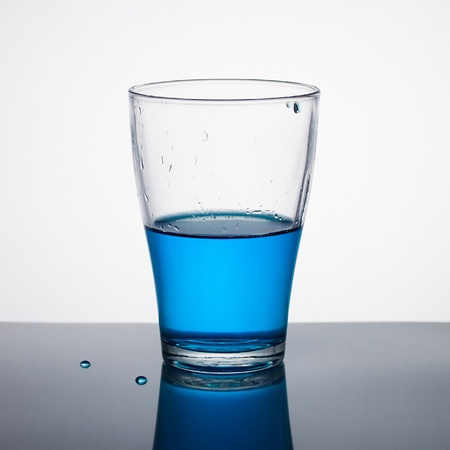 Glass half full of blue liquid on light background の写真素材