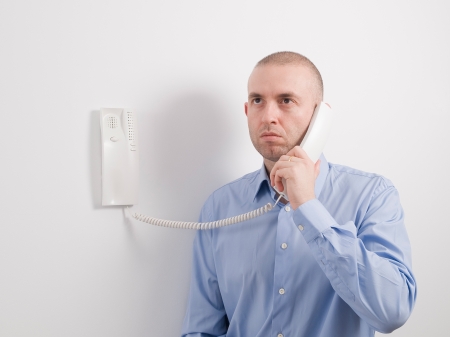 Caucasian man holding an intercom on a white wall 