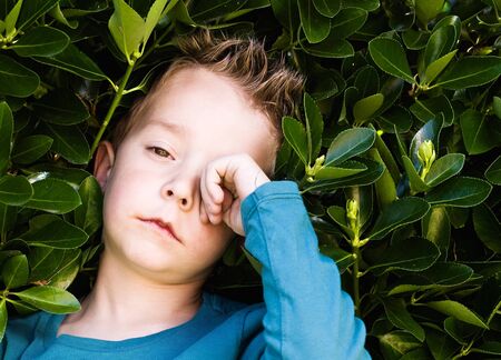 Blond boy rubbing his eyes. The child is sleepy and tired.の写真素材