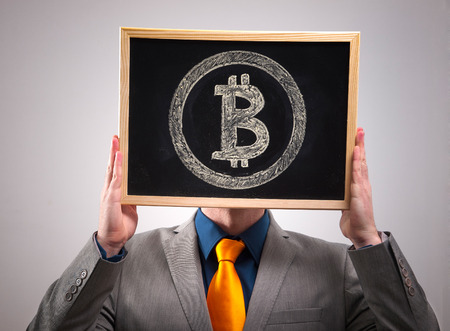 Businessman hiding his face behind bitcoin symbol and isolated on dark backgroundの写真素材