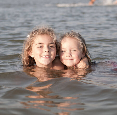 Two Little girls swimming at the beach and looking at camera.の写真素材