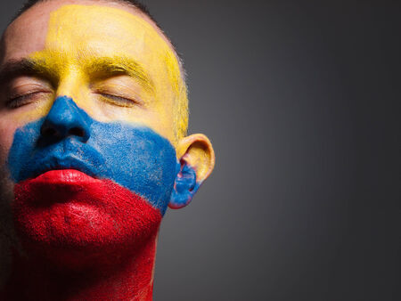 Man and his face painted with the flag of Colombia. The man has his eyes closed and photographic composition leaves only half of the face. の写真素材