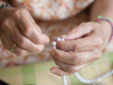 Hands of elderly woman threading a necklace. Hands macro detail.の写真素材