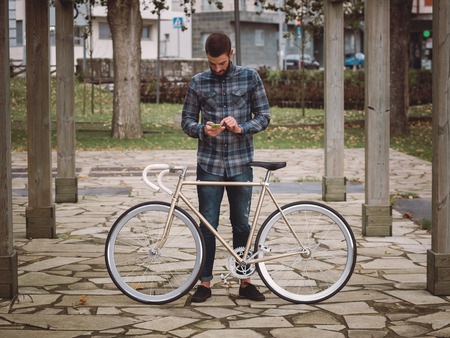 Hipster man with a fixie bike and smartphone in a park outdoorsの写真素材