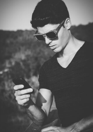 Model man portrait with wooden sunglasses outdoors in a sunny day. Man is using a smartphoneの写真素材