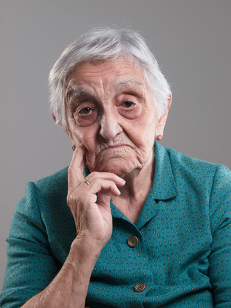 Elderly woman portrait in a studio shot. Old woman had her hand on chin and sadの写真素材