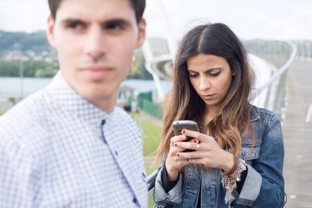 Woman distracted looking at her smart phone. The woman is not aware of her boyfriend.の写真素材