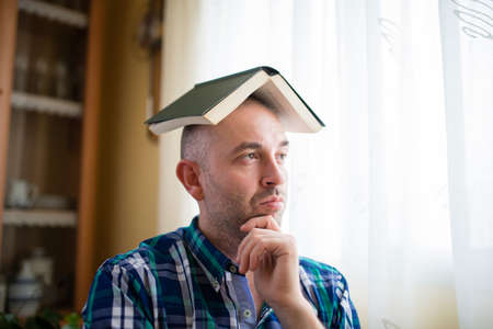 Adult man with a book on his head. He is thoughtfully