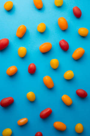Elongated cherry tomatoes of different colors (red, yellow, and orange) over blue backgroundの写真素材