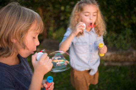 Boy and girl blowing soap bubbles outdoorsの写真素材