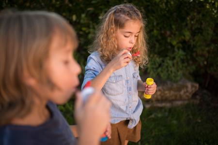 Boy and girl blowing soap bubbles outdoorsの写真素材