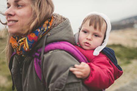 Mother carrying her child in a backpack outdoors in a cloudy dayの写真素材