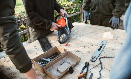 Team work of mechanics in workshop fixing a chainsaw for cutting trees in the forest. Agriculture, forest exploitation and field use concepts.の写真素材