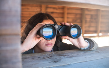 Girl in nature with binoculars doing outdoors activities. Searching, sightseeing, tourism, discover and birdwatching concept.の写真素材